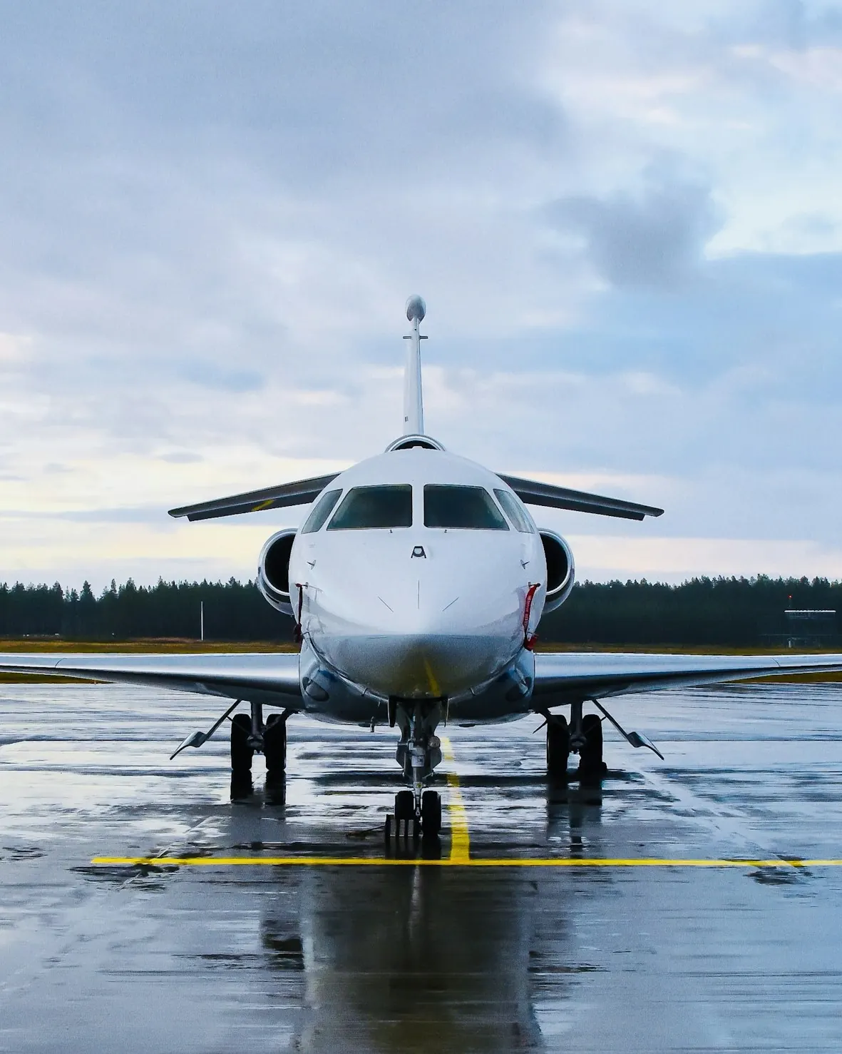 Large-cabin business jet parked nose-on on a wet apron under cloud