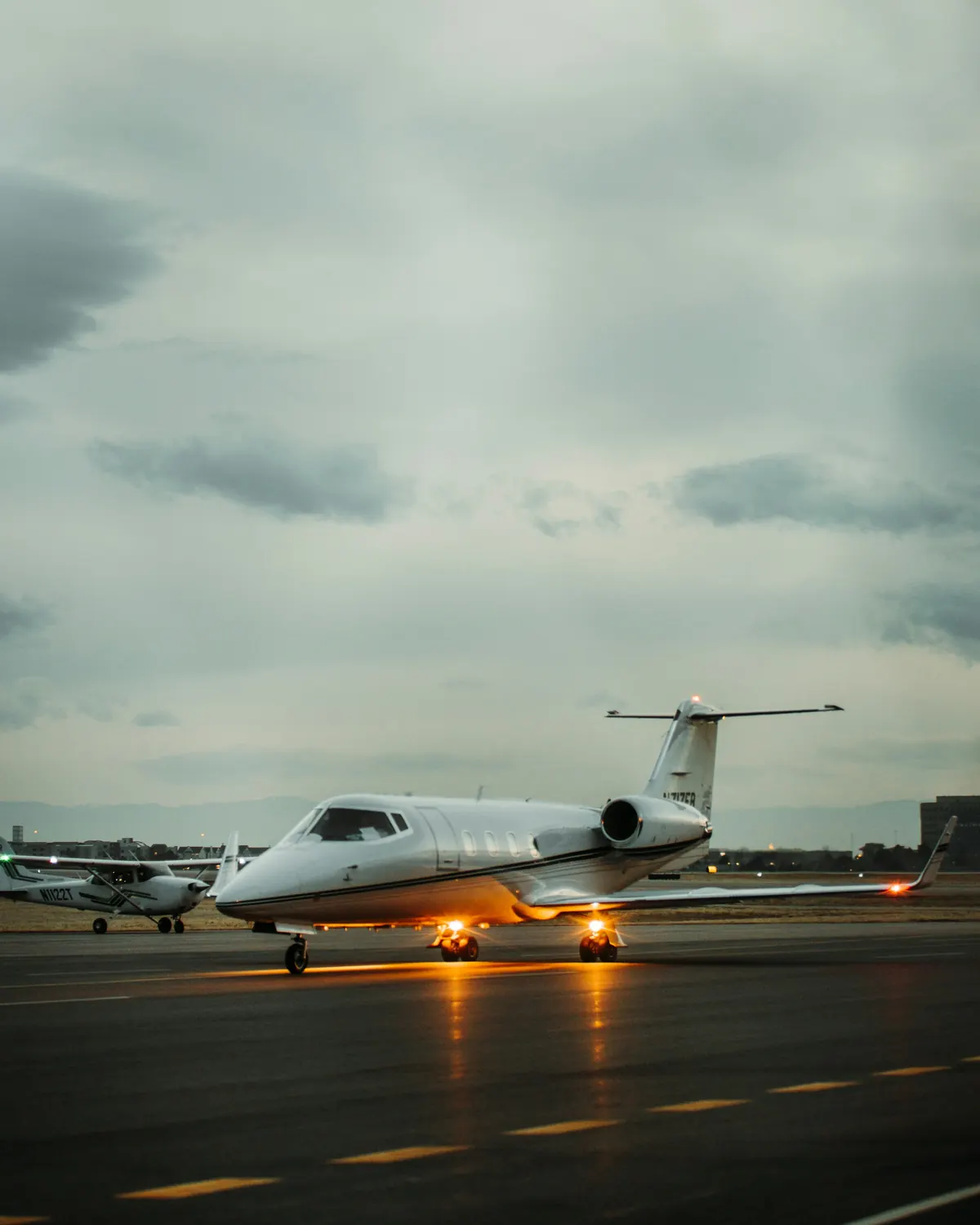 Business jet with its lights on taxiing across a wet ramp under heavy cloud