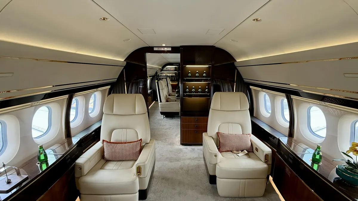 Empty cream leather seats facing each other in a long, quiet jet cabin