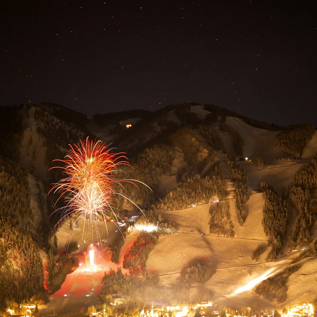 Fireworks over Aspen Mountain on a winter night, with the town lights below