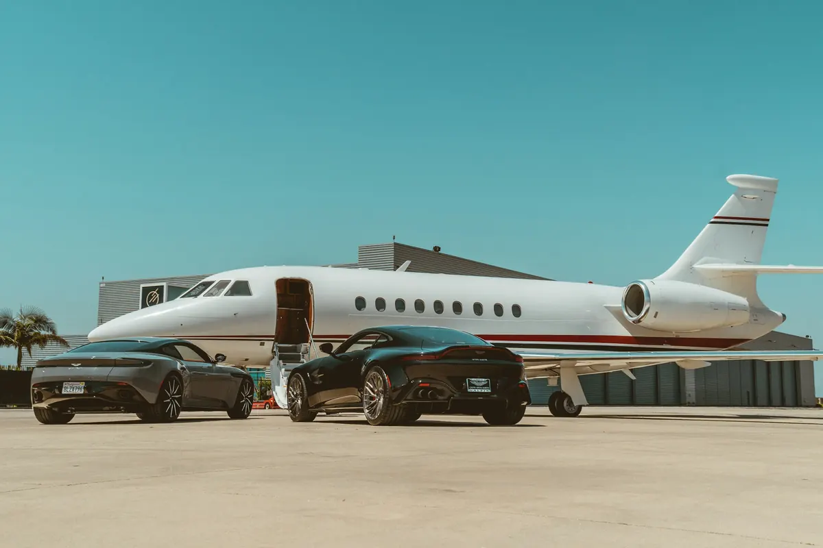 Business jet with its stairs down beside two sports cars on a sunny ramp