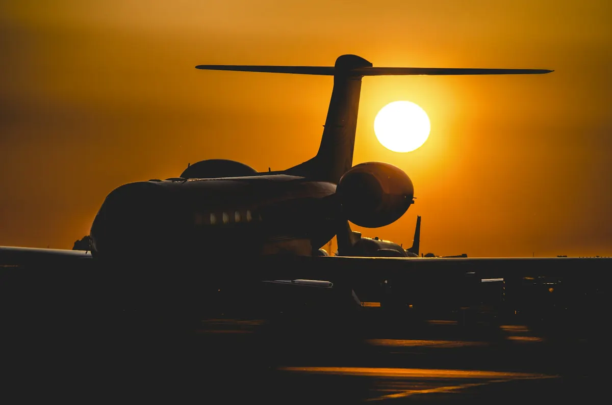 Long-range business jet in silhouette against a low orange sun on the apron